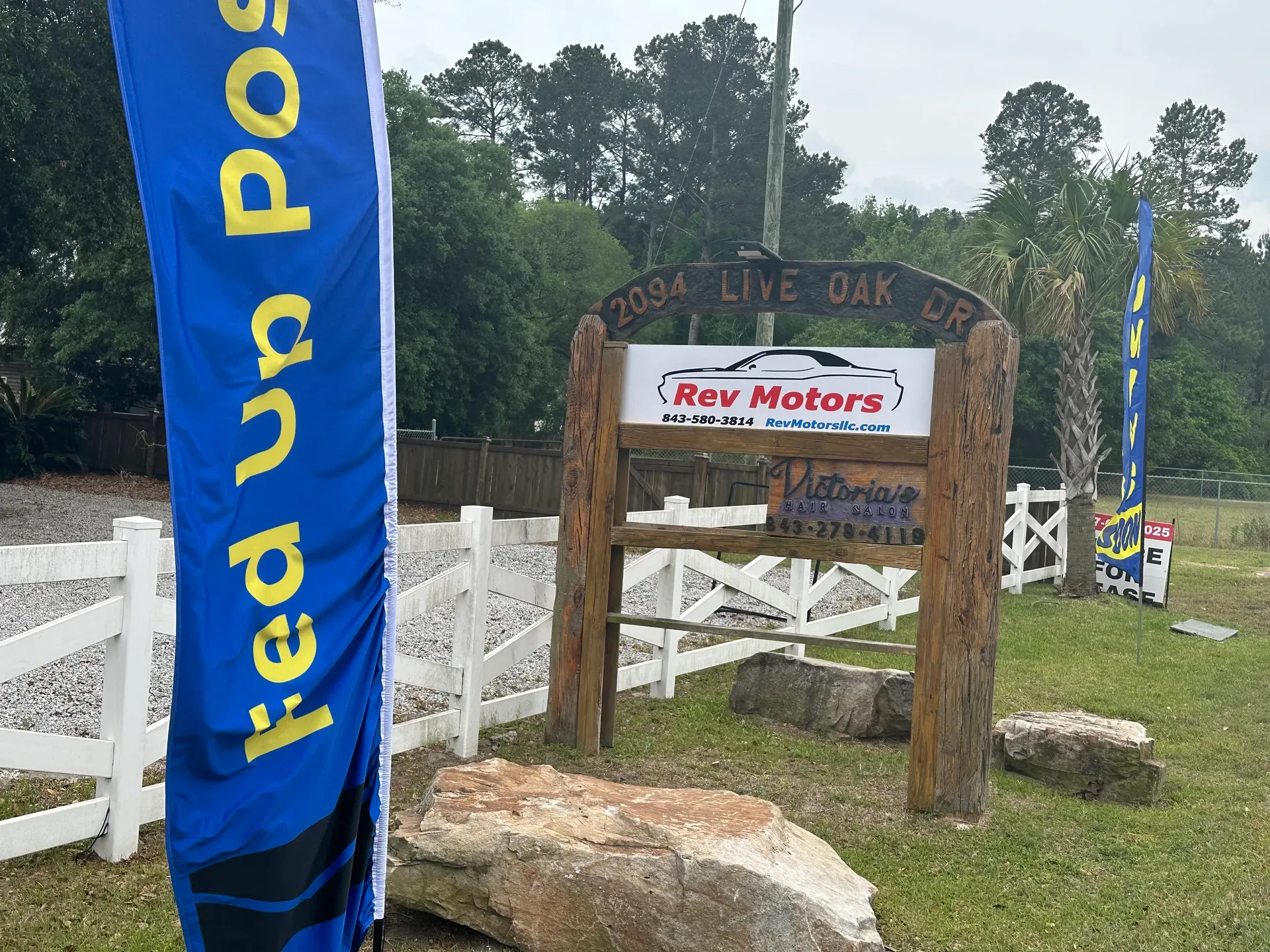 The Fed Up Postal entrance at 2094 Live Oak Drive in Moncks Corner, marked by a wooden archway with Rev Motors and Victoria's signage and blue Fed Up flags