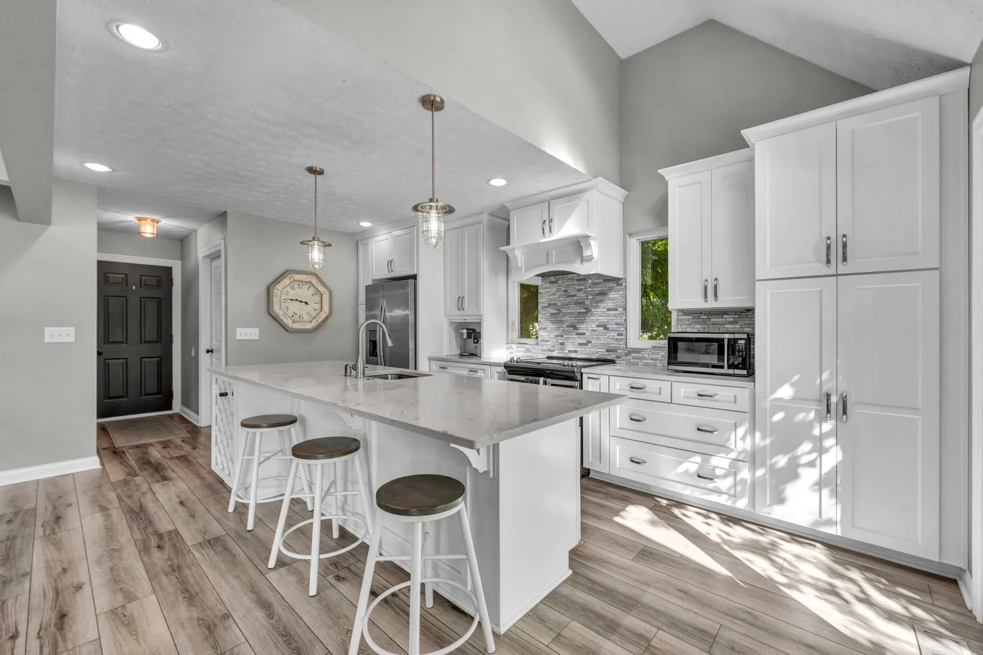 Kitchen with white cabinetry, stone backsplash, and a large center island