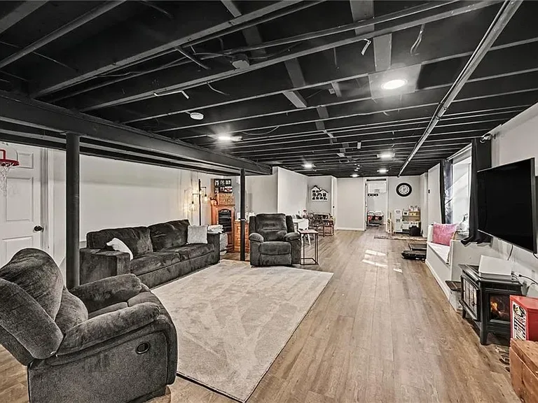 Lower level lounge with exposed painted ceiling and light wood flooring at the Merriam home