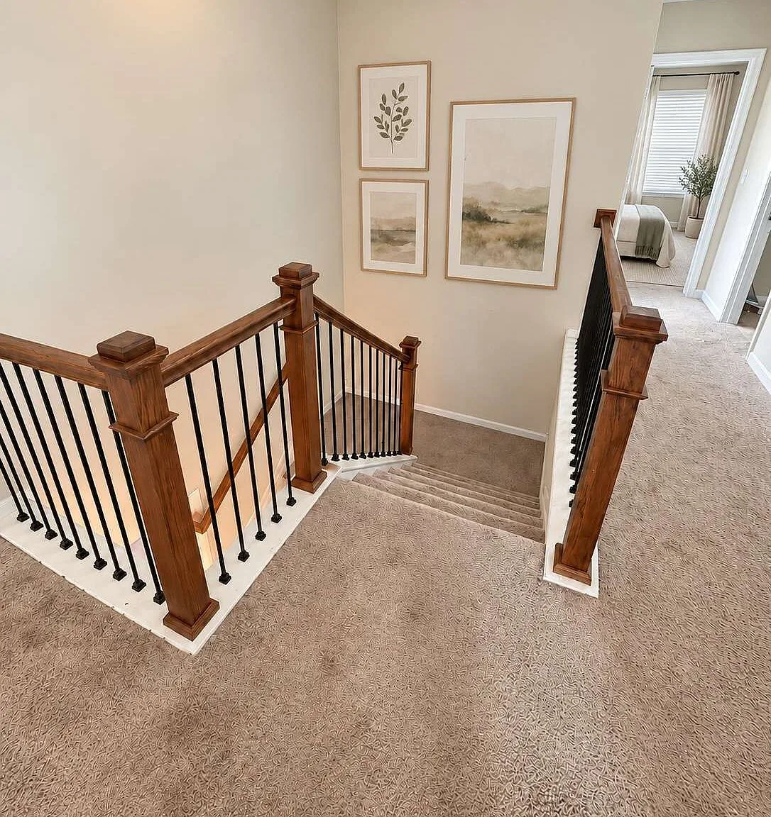 Carpeted staircase with wooden handrails and black metal balusters seen from the upper landing