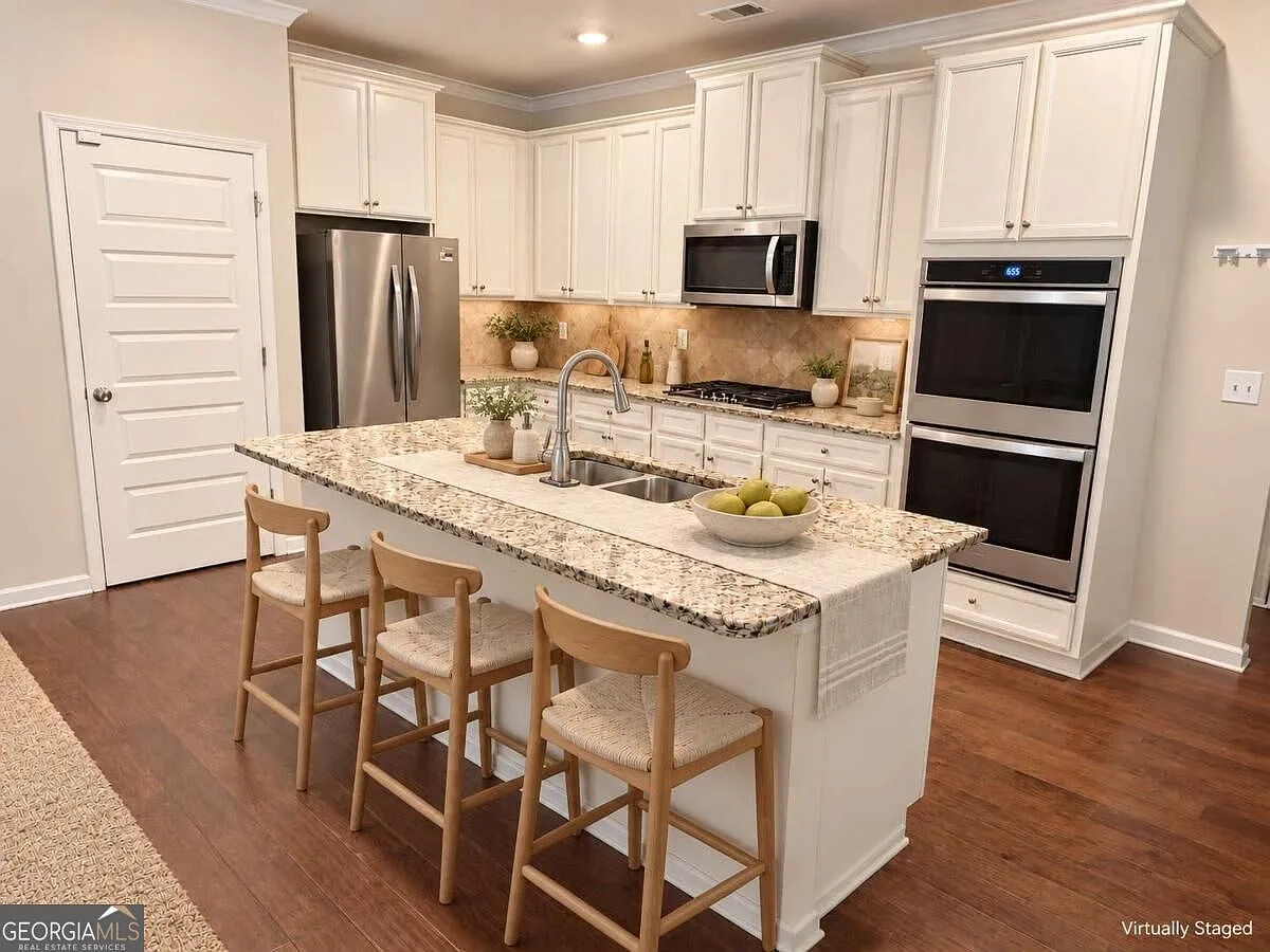 Kitchen island with granite countertops, white cabinetry and stainless steel double ovens