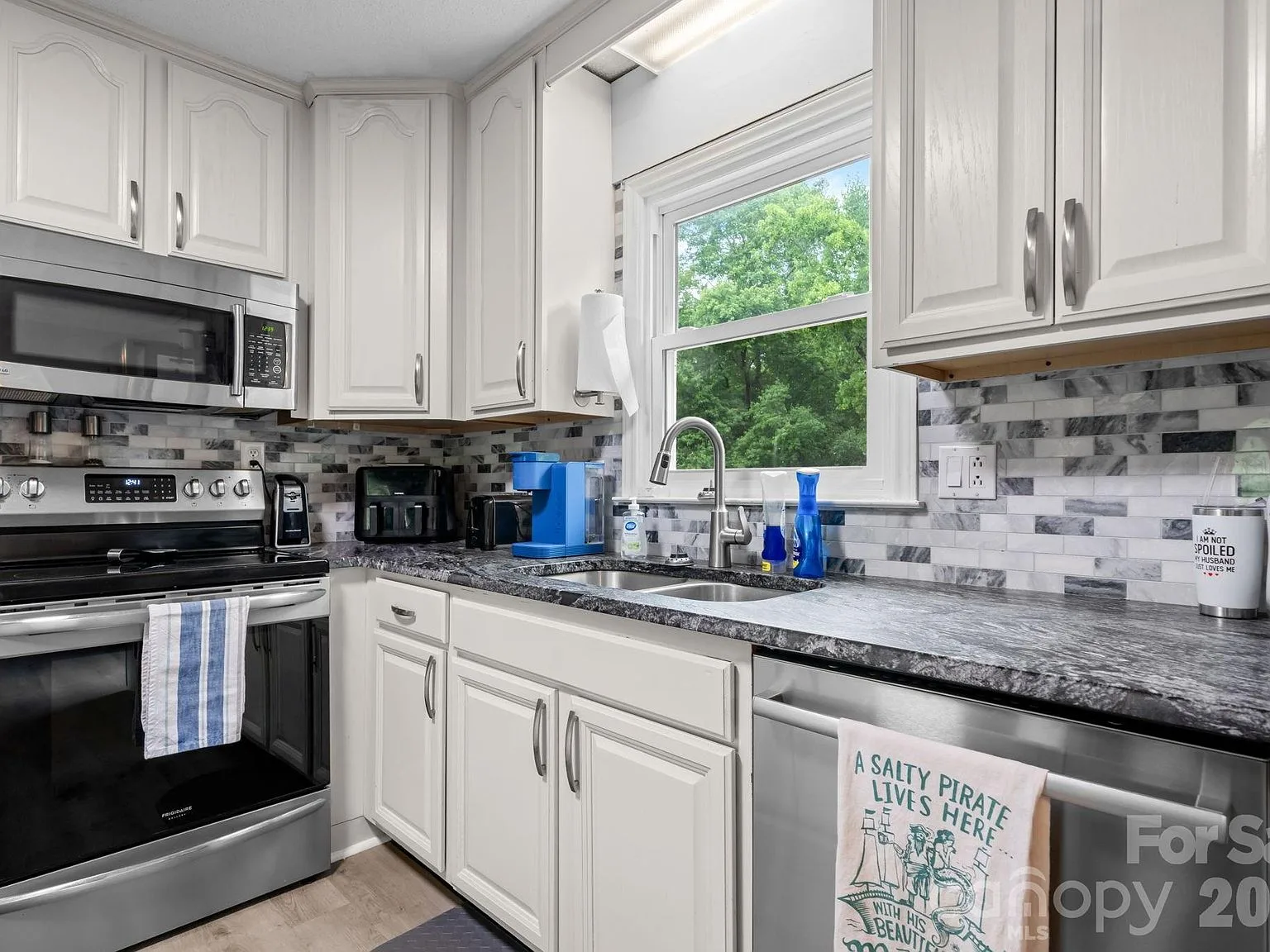 Kitchen sink area with white painted cabinets, leathered granite, and a gray tile backsplash above the sink window