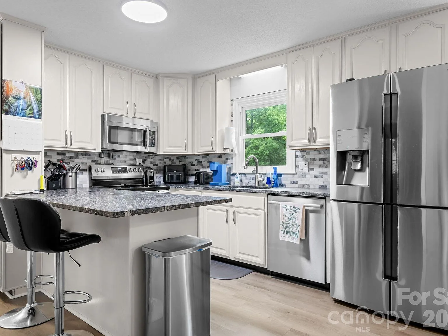 Kitchen with white cabinetry, leathered granite countertops, stainless steel appliances, and tile backsplash