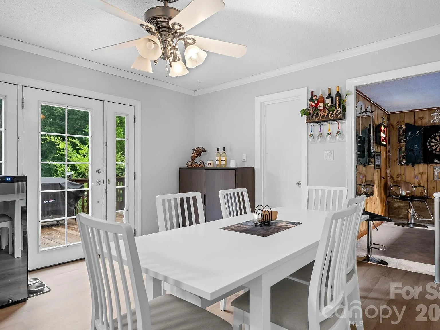 Dining area with a single door with glass panels on either side opening toward the deck, white table and chairs, and hardwood-style flooring