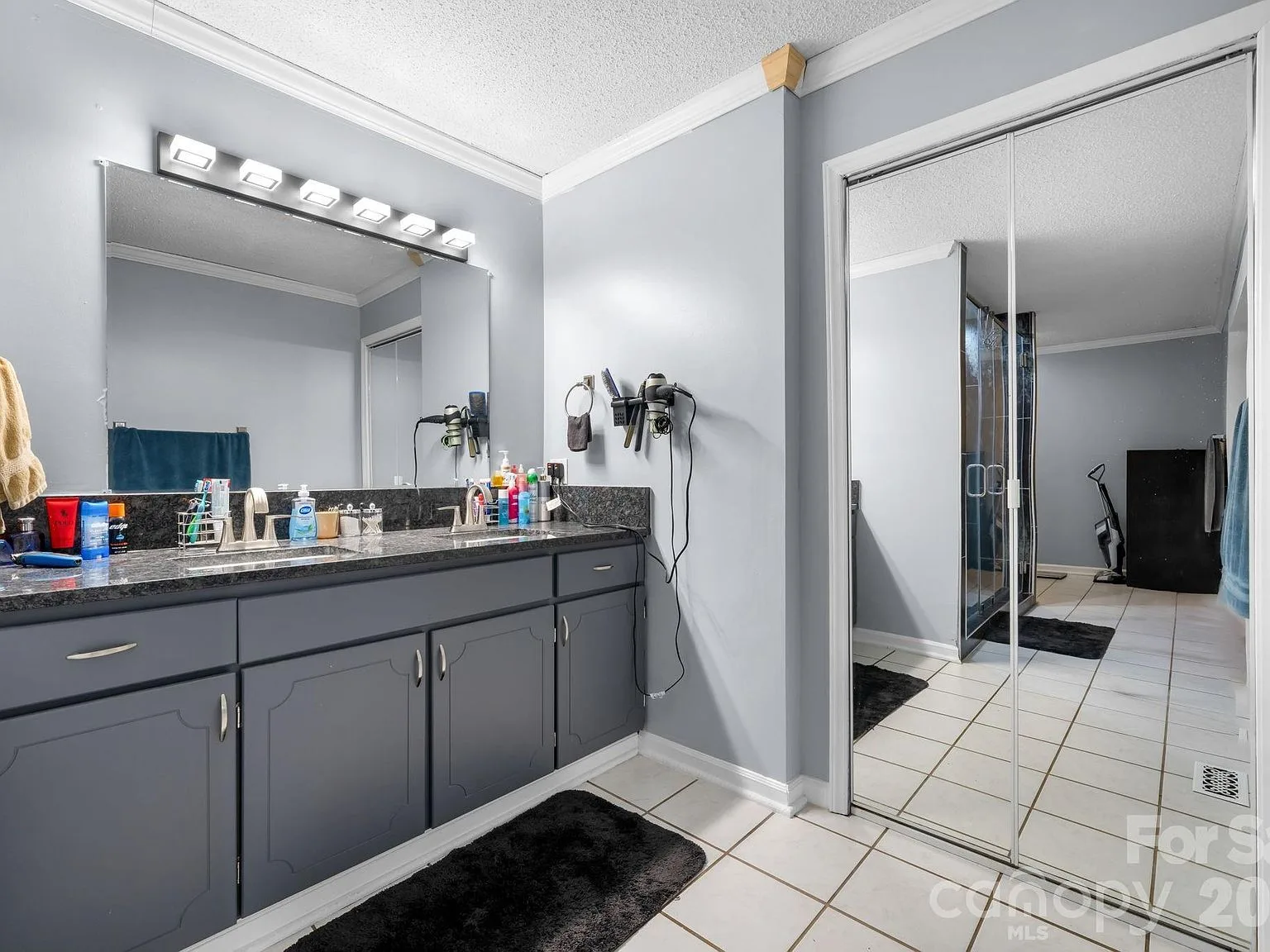 Primary bath double vanity with dark grey cabinets, dark granite counters, and a large mirror with light bar