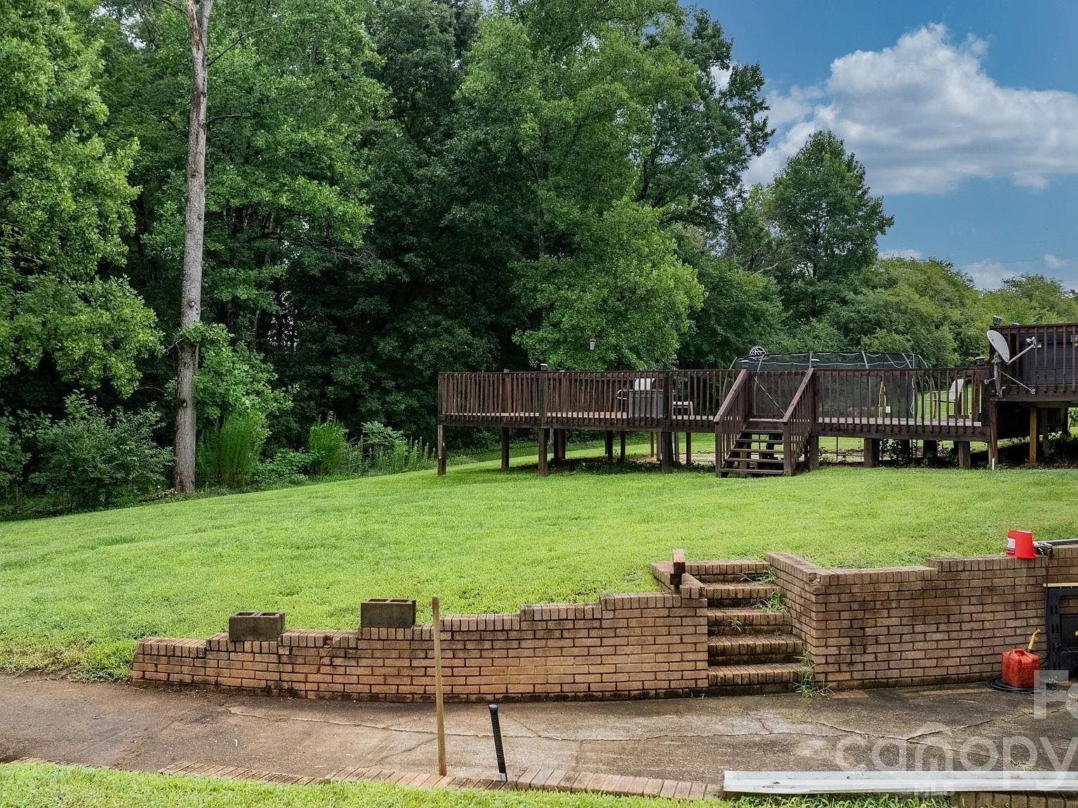 Large wood deck off the back of the home with stairs down to a brick retaining wall and patio