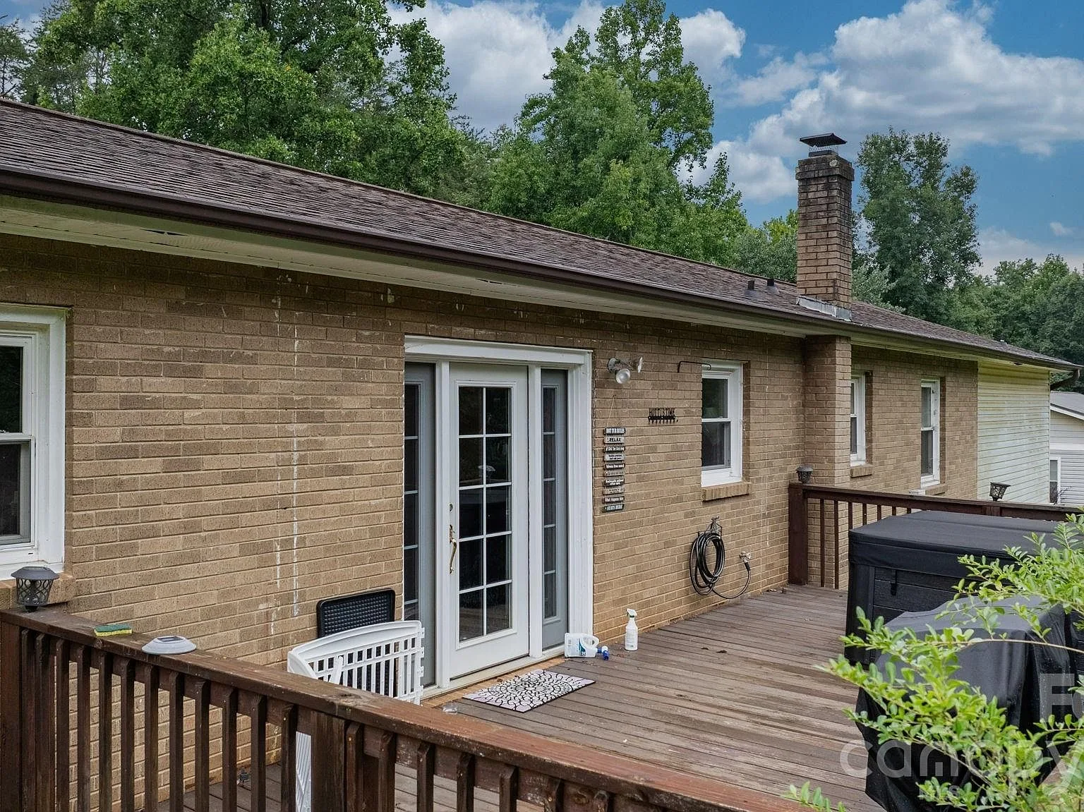 Rear of the home with wood decking, a brick facade, and a single back door flanked by glass side panels on a sunny day