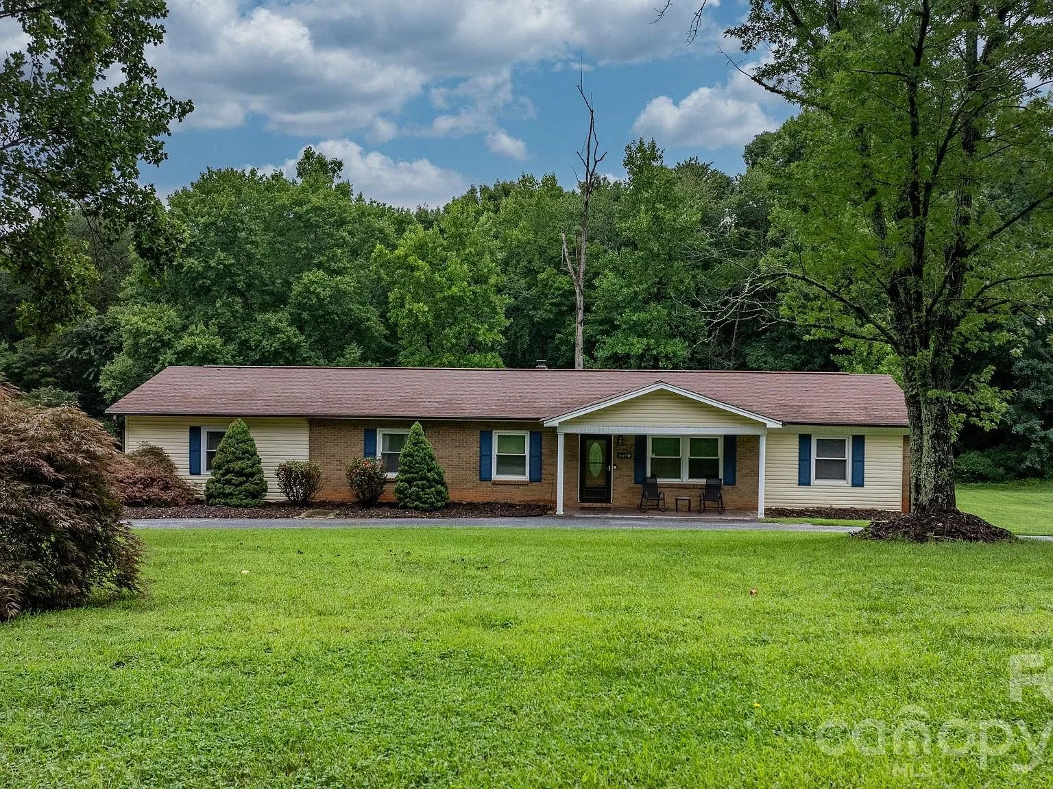 Front facade of the ranch-style home at 4690 Worth Pl in Granite Falls, North Carolina, with beige siding, brick veneer, blue shutters, and a green front yard