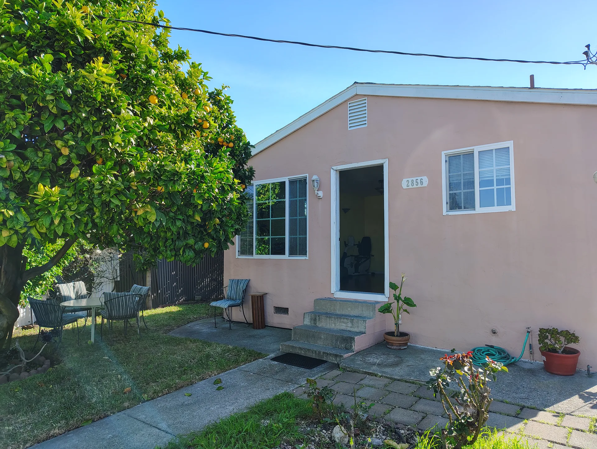 Front exterior of 2856 15th Street, San Pablo, CA 94806, a single-story cottage with light pink stucco siding and white trim, with a lemon tree in the foreground