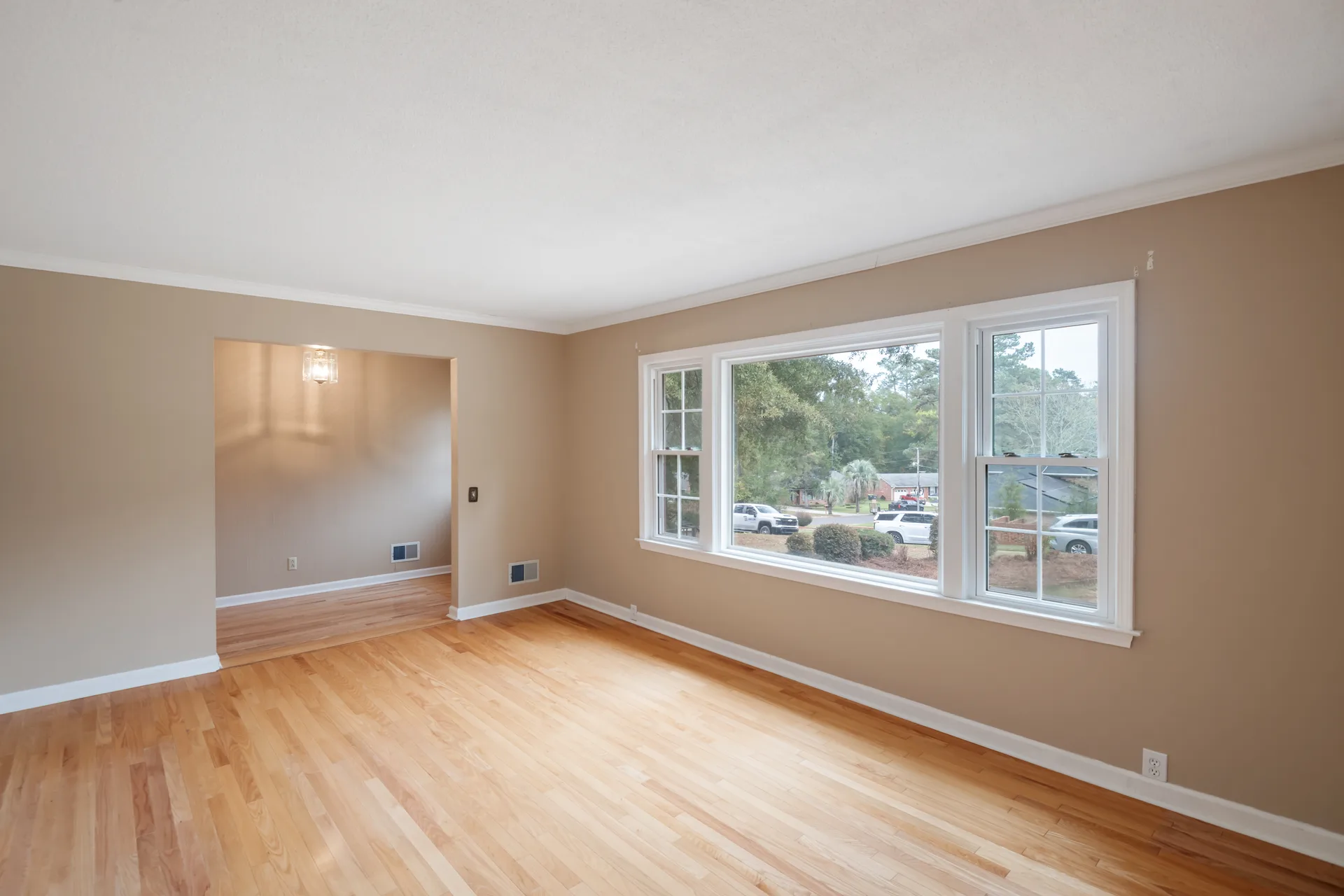 Bright living room with polished hardwood floors, crown molding, and large windows