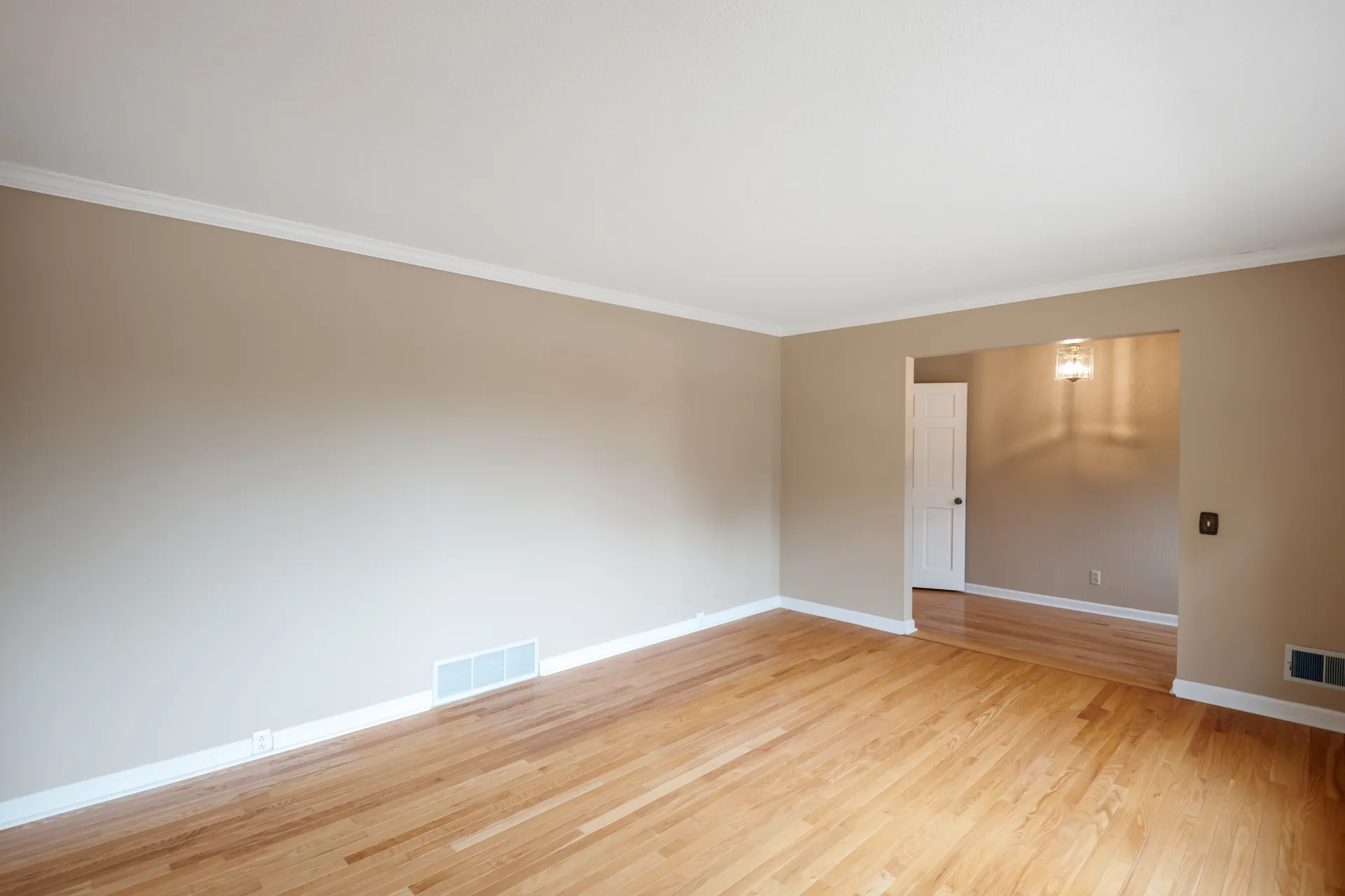 Wide living room with hardwood floors, white baseboards, and crown molding