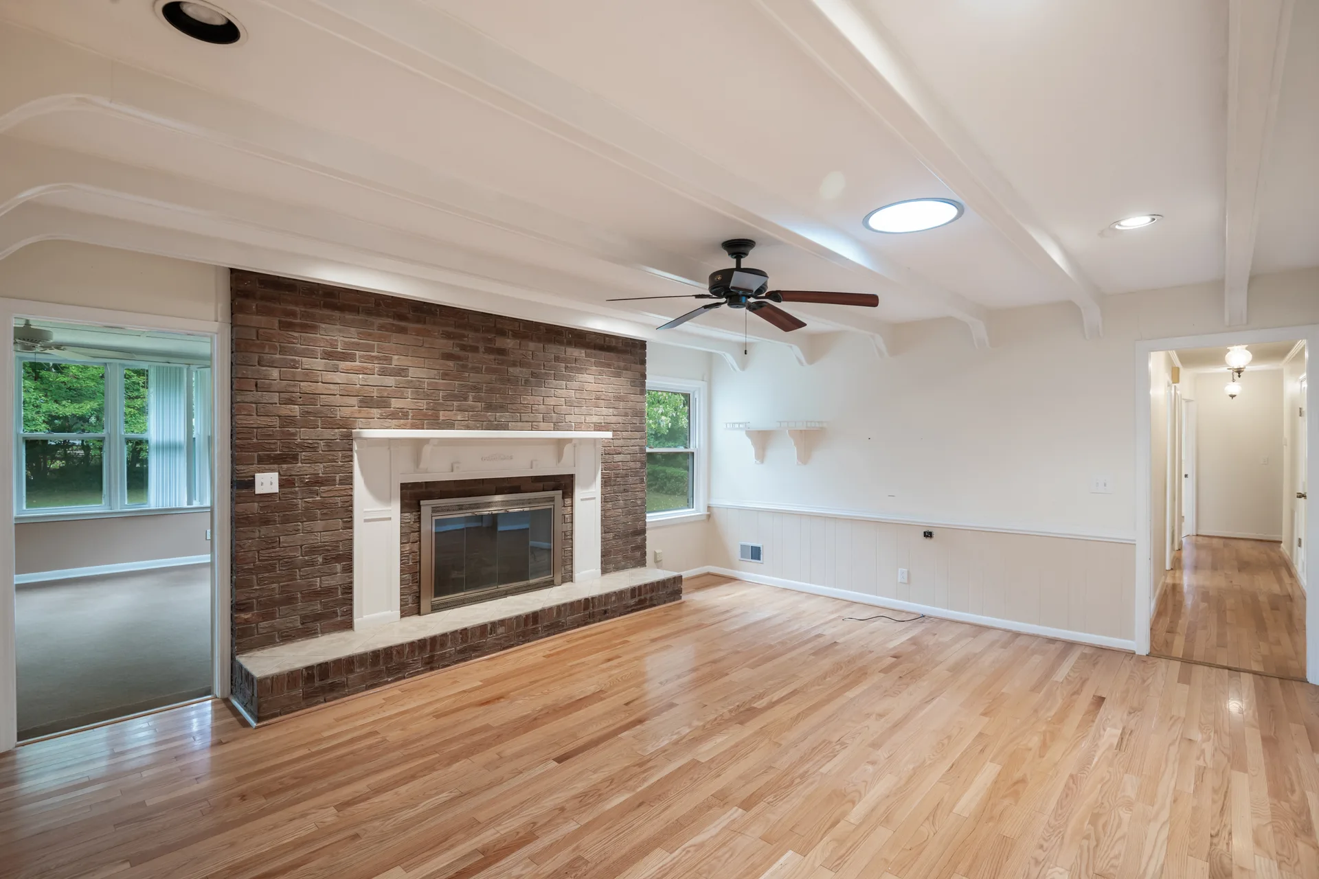 Living room with a large brown brick fireplace, white mantel, and light hardwood floors