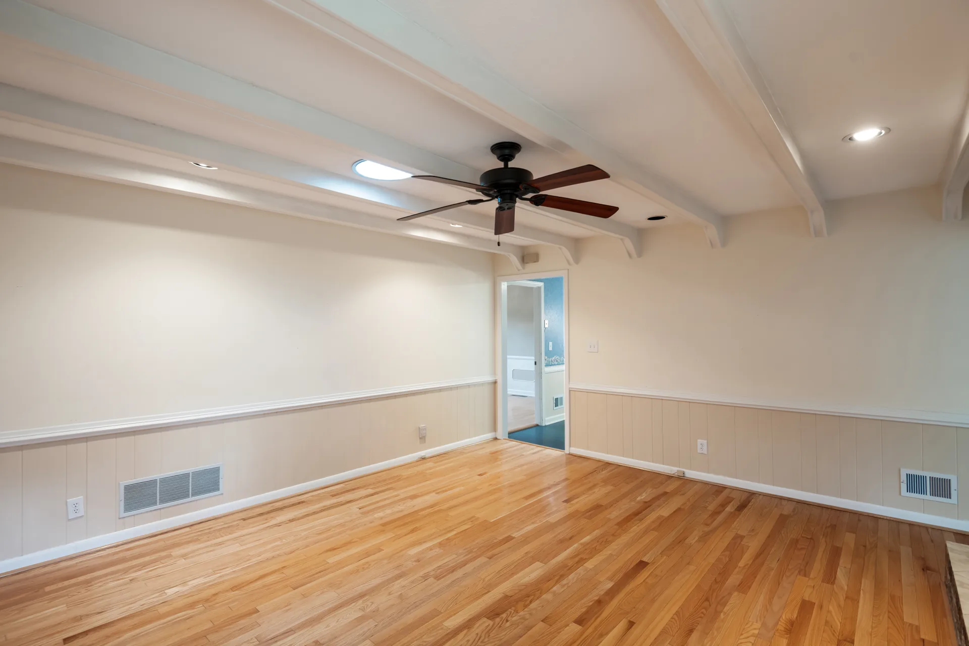 Living room with exposed painted beams, wainscoting, and hardwood floors
