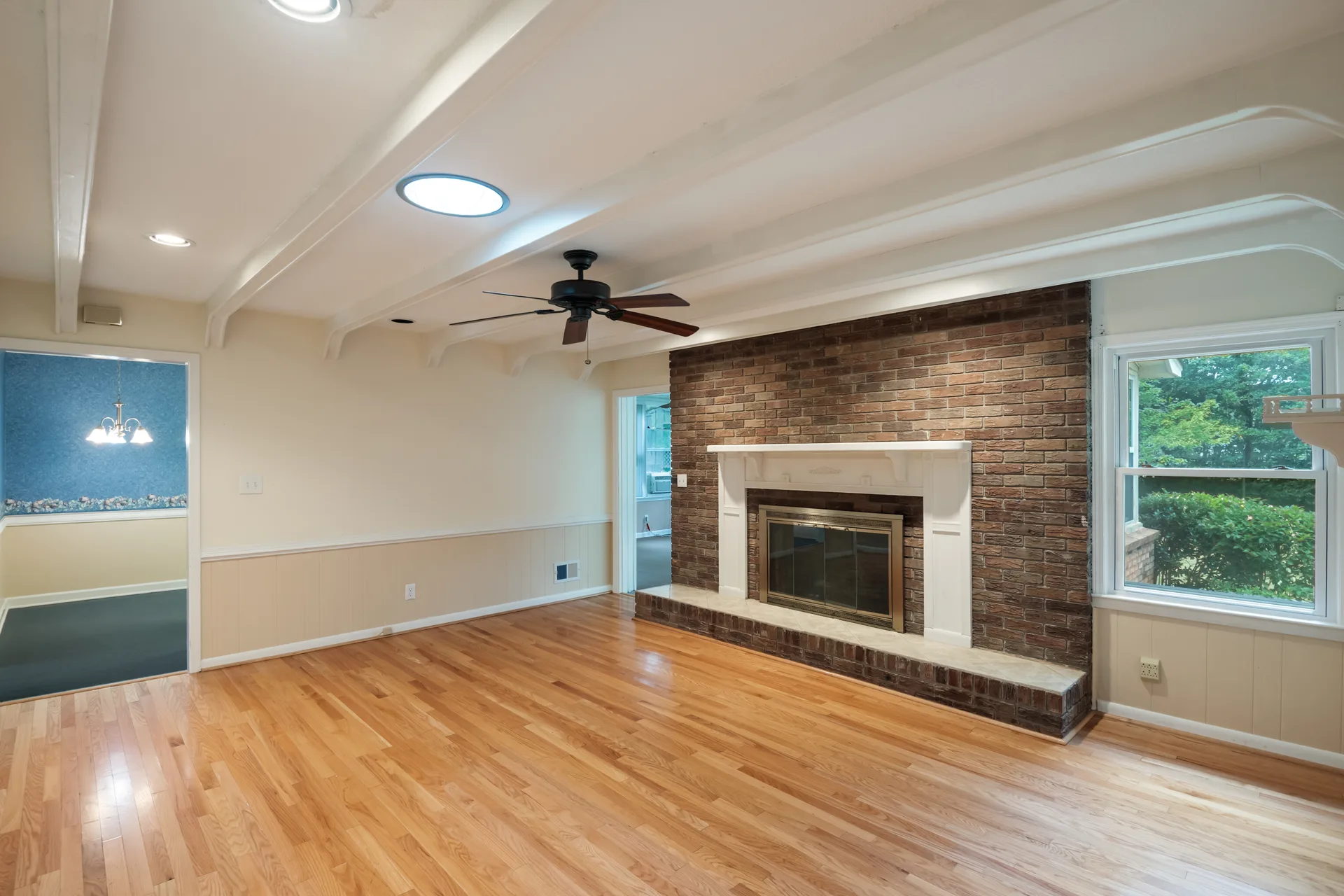 Living room with a floor-to-ceiling brick fireplace, white mantel, and exposed ceiling beams