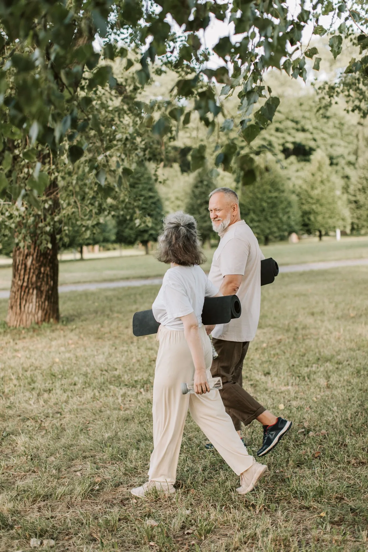 An older couple walking through a park with yoga mats, staying active together