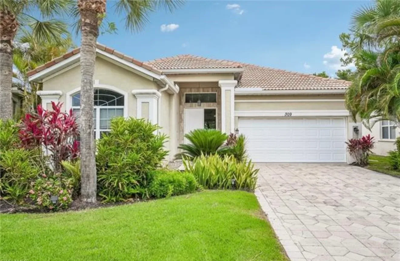 Front entry and garage of the stucco home at 309 Harvard Ln, Naples, with a tiled roof and palm landscaping