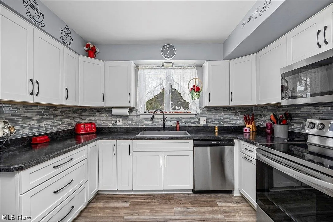 Straight-on view of the updated kitchen with dark granite counters and mosaic backsplash