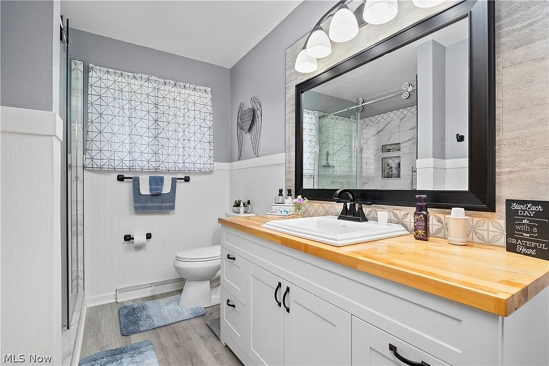 Updated bathroom with white vanity, butcher-block counter, and black framed mirror