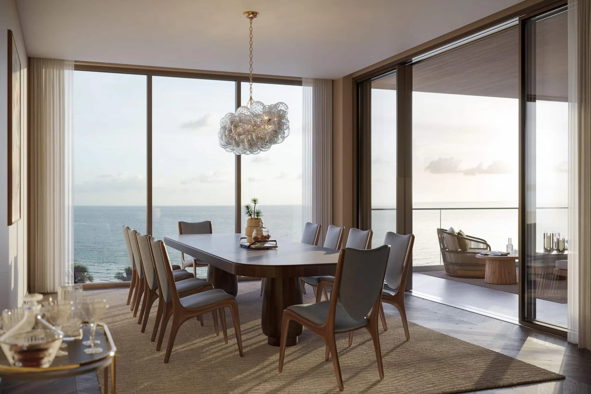 Comedor en Rosewood Residences Naples con vista al mar, mesa de pedestal de madera oscura y pisos de madera espiga