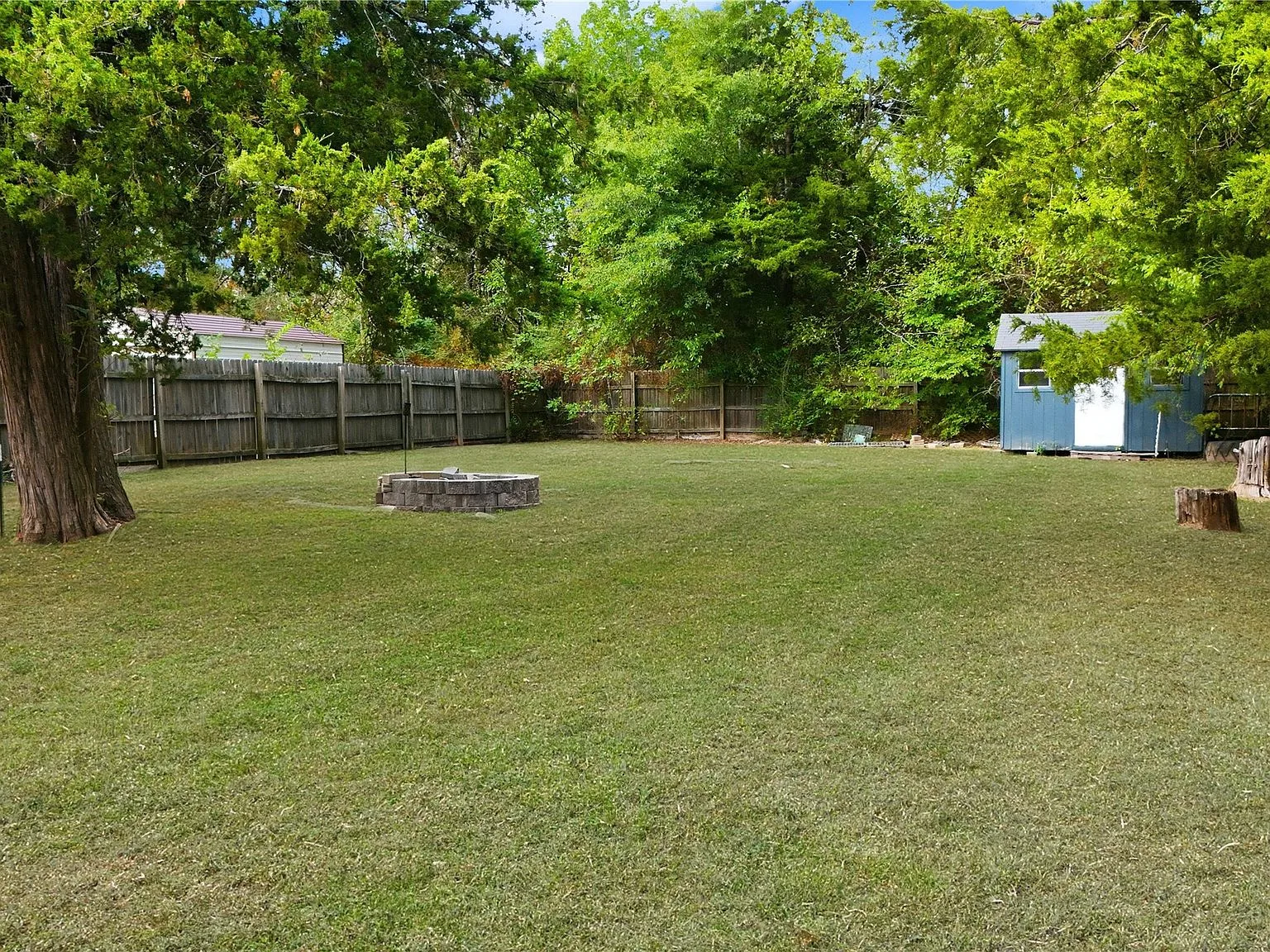 Stone fire pit on the lawn with mature trees and dappled shade