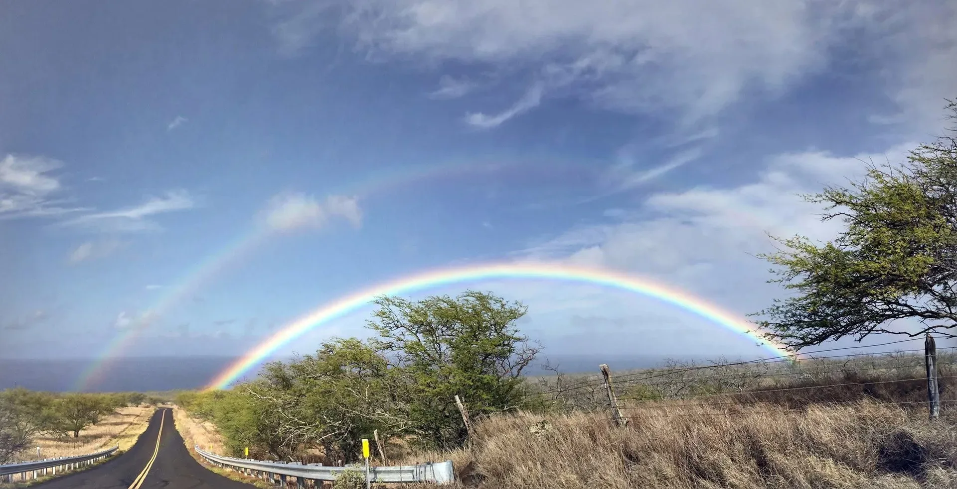 Akoni Pule Highway on Hawaiʻi Island, with a rainbow above the coastal landscape.