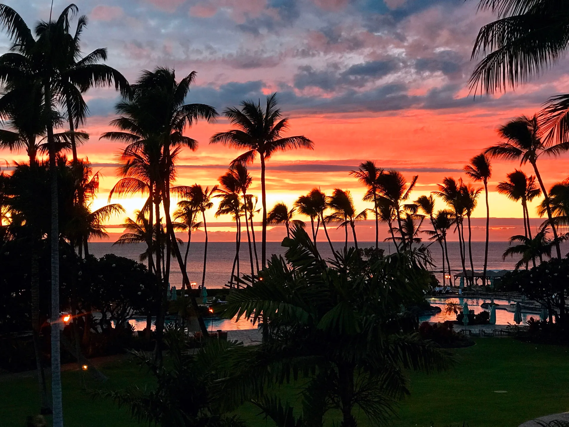 Sunset over the shoreline at the Mauna Lani Resort on the Kohala Coast, with palm trees silhouetted against a golden sky