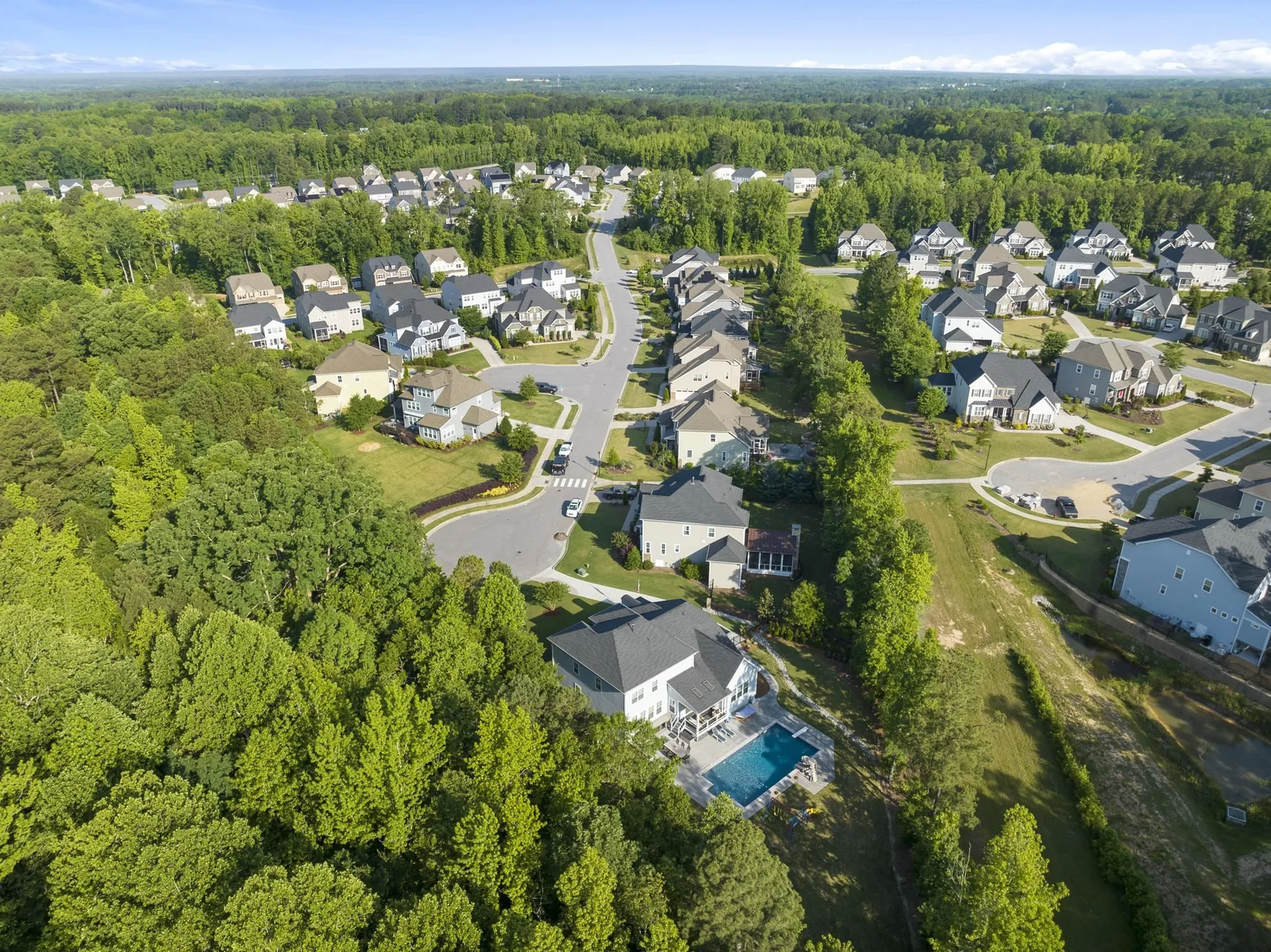 Drone view of a home with an in-ground pool and green streets in Salem Village, Apex NC