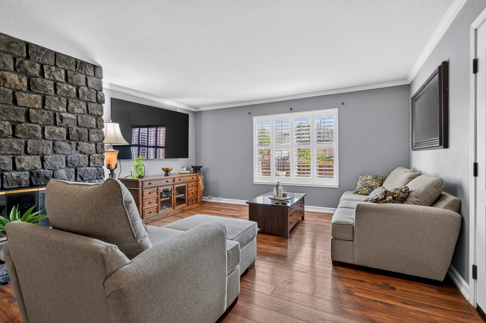 Tidy living room with gray sofa, stone fireplace, and warm hardwood floors, photographed for a Castro Valley home sale.