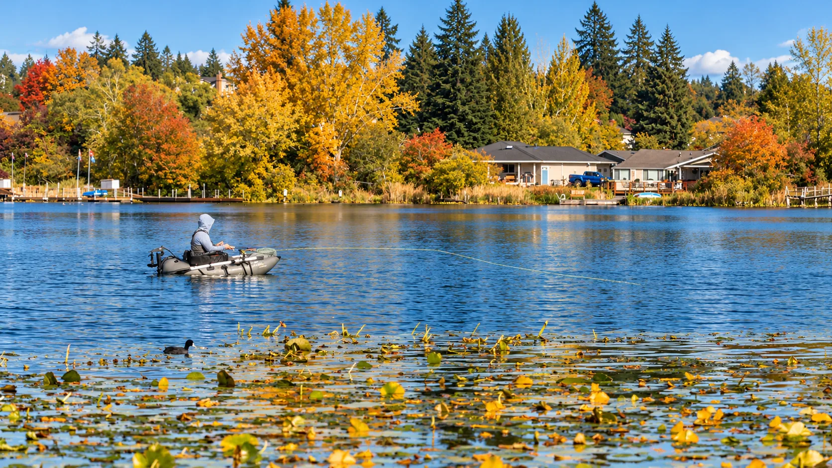 Blackmans Lake in autumn in Snohomish, Washington, with a person fishing from a small boat among lily pads and vibrant fall foliage along the shore