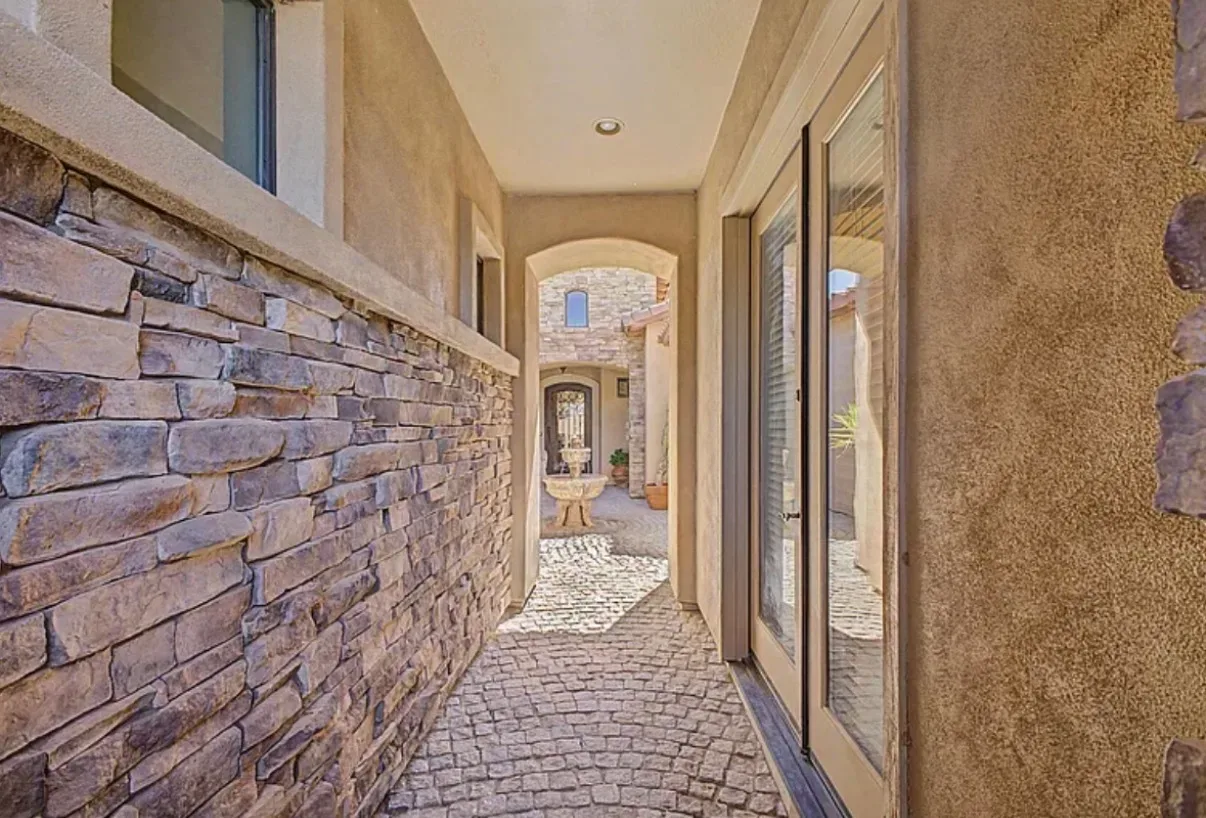 Stone courtyard walkway with stucco walls and a water fountain in the distance