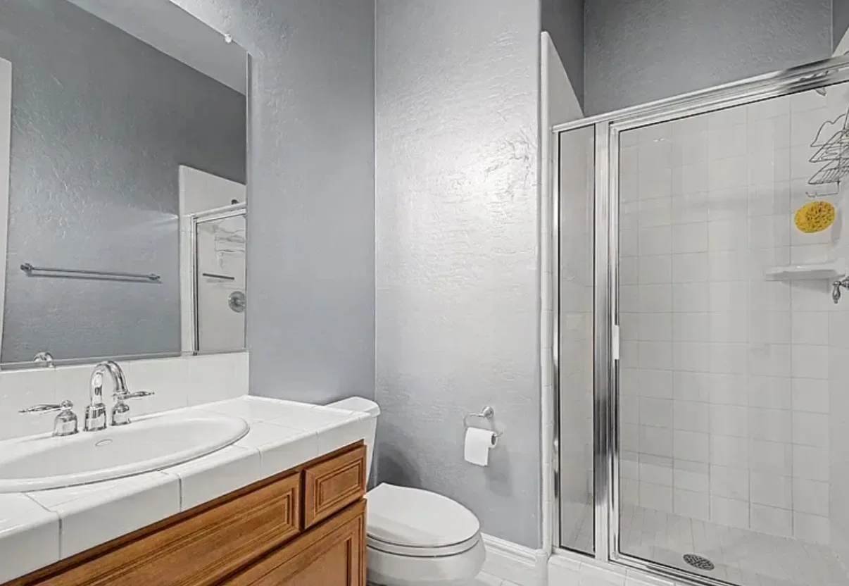 Bathroom with a wood vanity, tiled countertop, and glass shower