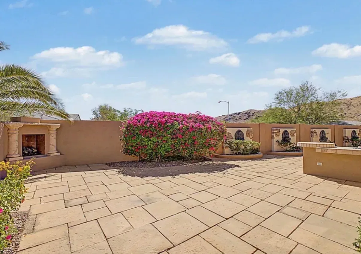 Backyard patio with a stone fireplace and bougainvillea under a clear sky