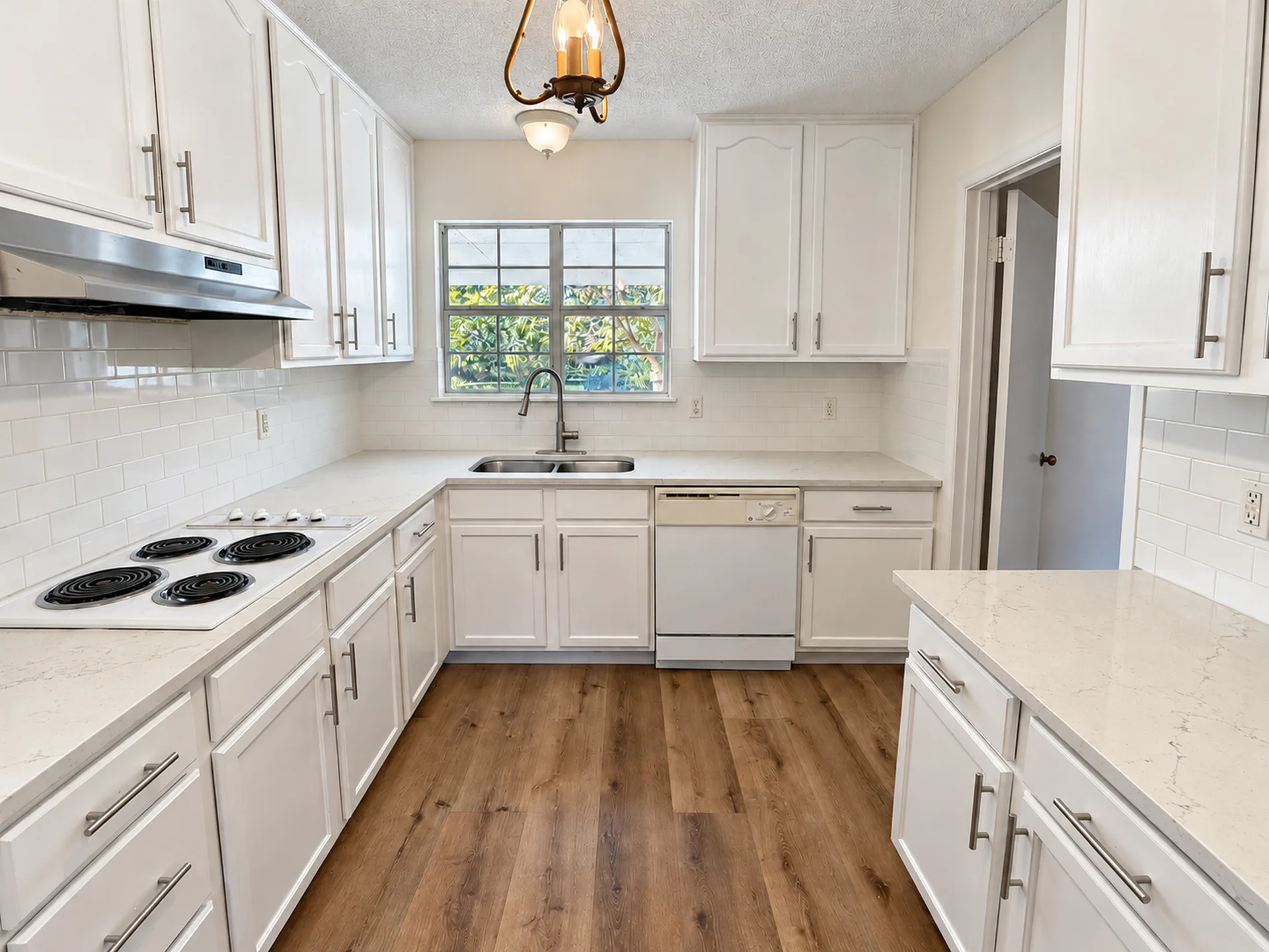 Updated galley kitchen with white shaker cabinetry, a subway tile backsplash, and light countertops