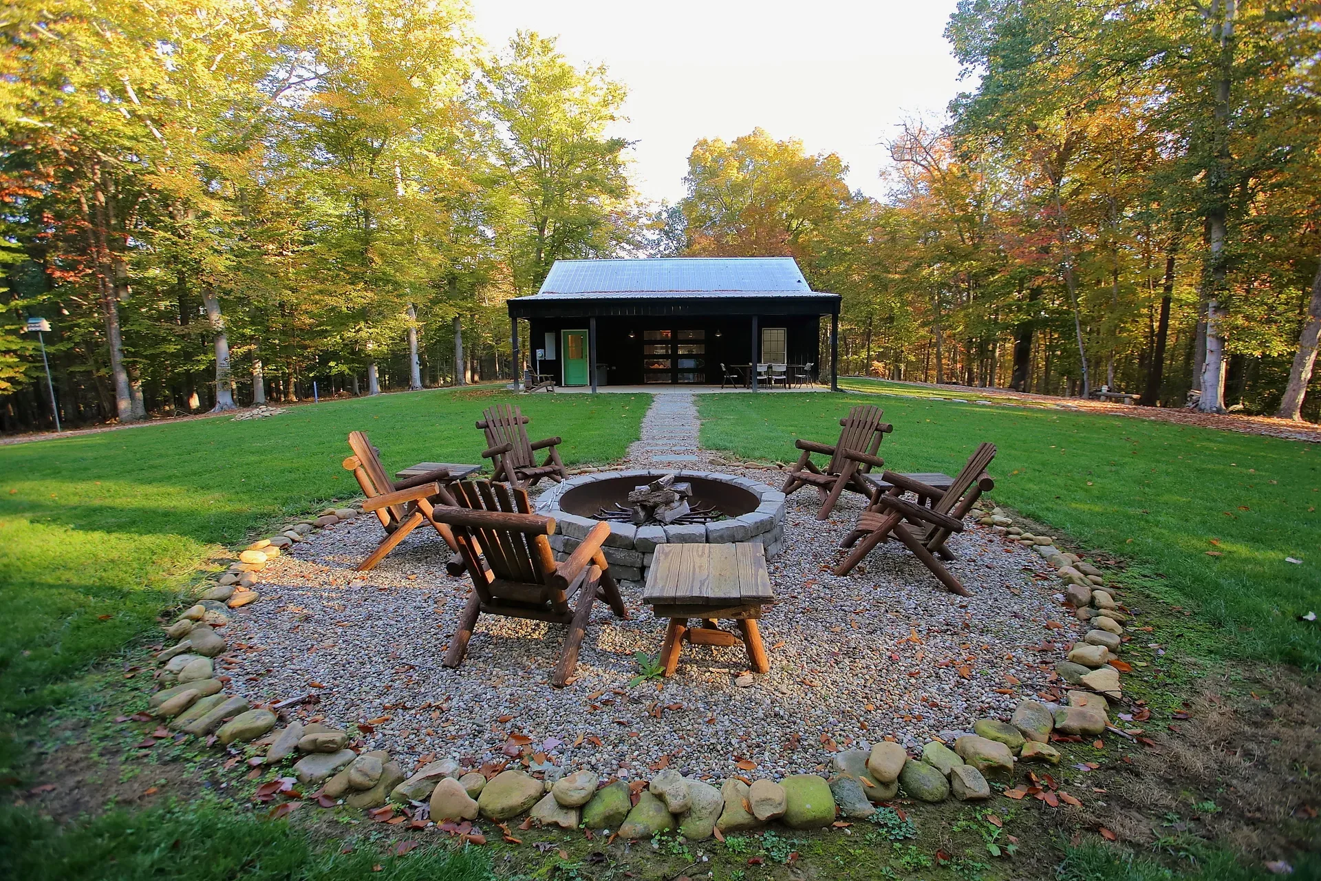Backyard fire pit with Adirondack chairs beside the barndominium and surrounding woods