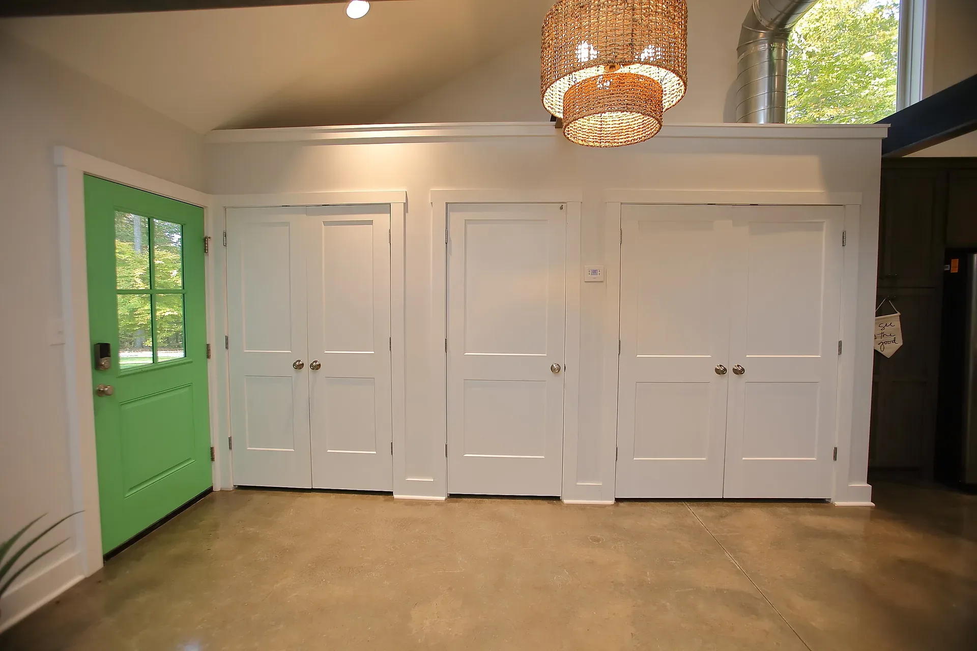 Entryway with bright green front door and woven chandelier