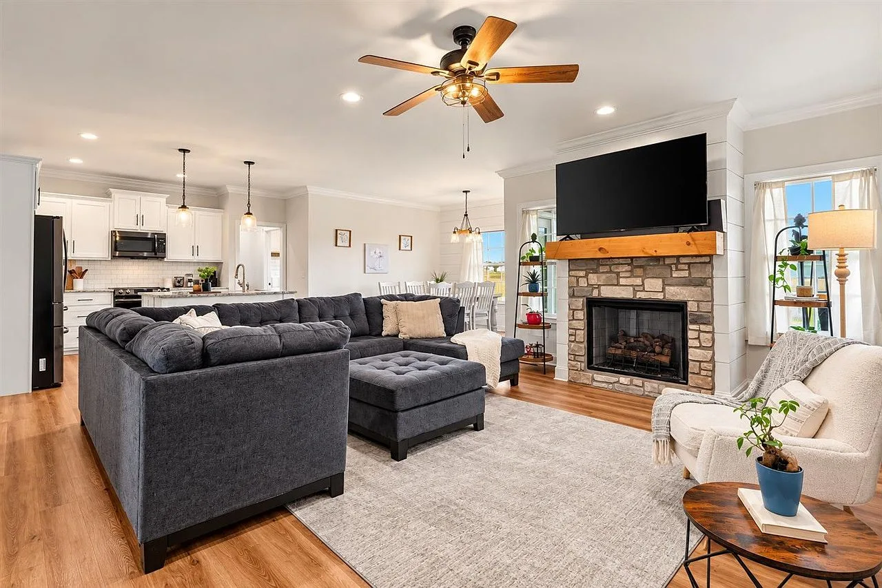 Open-concept living room flowing into the kitchen with a stone fireplace and white shiplap