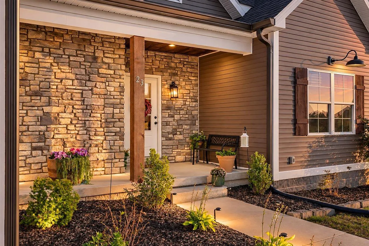 Covered front entryway with stone veneer, wood porch post, and warm landscape lighting