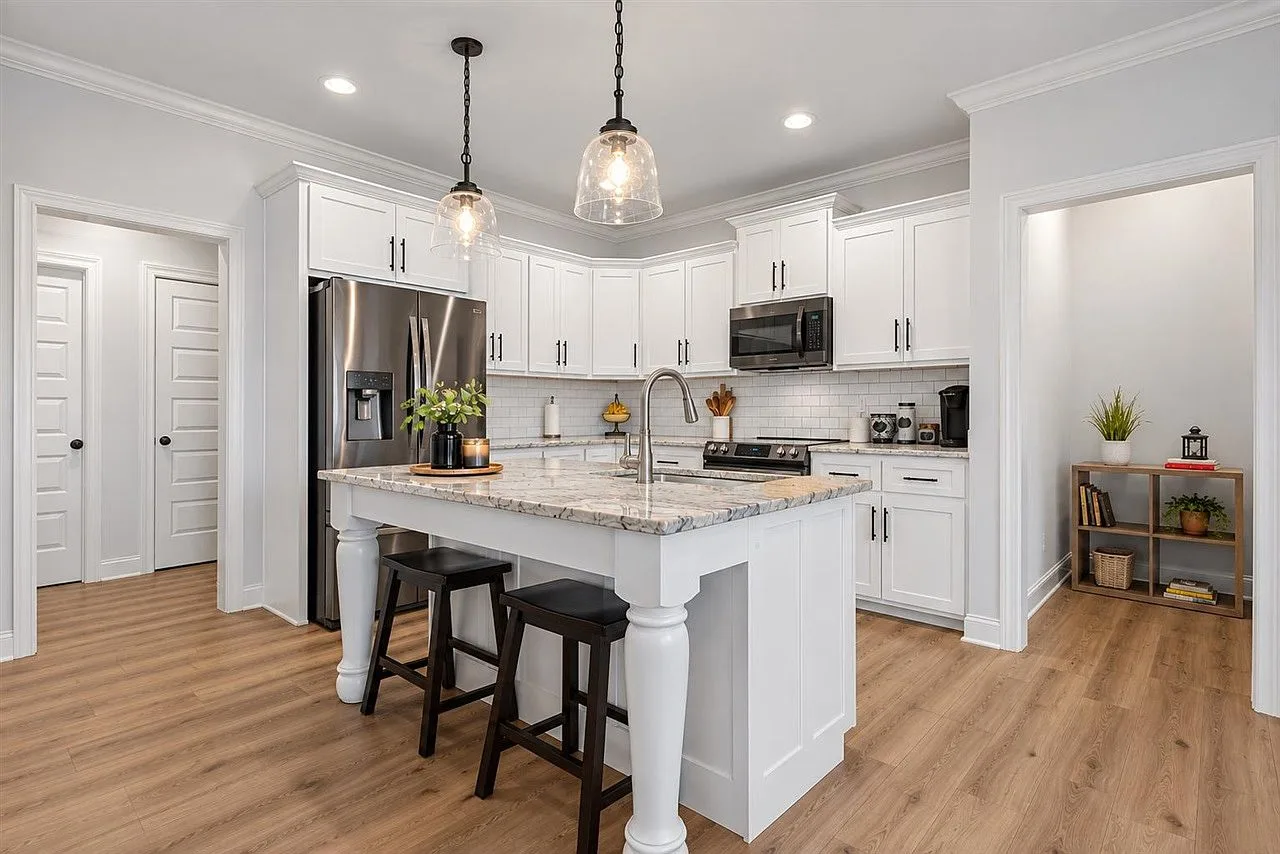 Wide kitchen view with white cabinetry, a granite island, and pendant lights