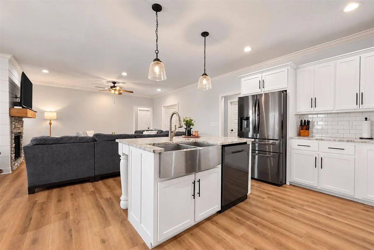 Kitchen opening to the living room with a farmhouse sink and stone fireplace beyond
