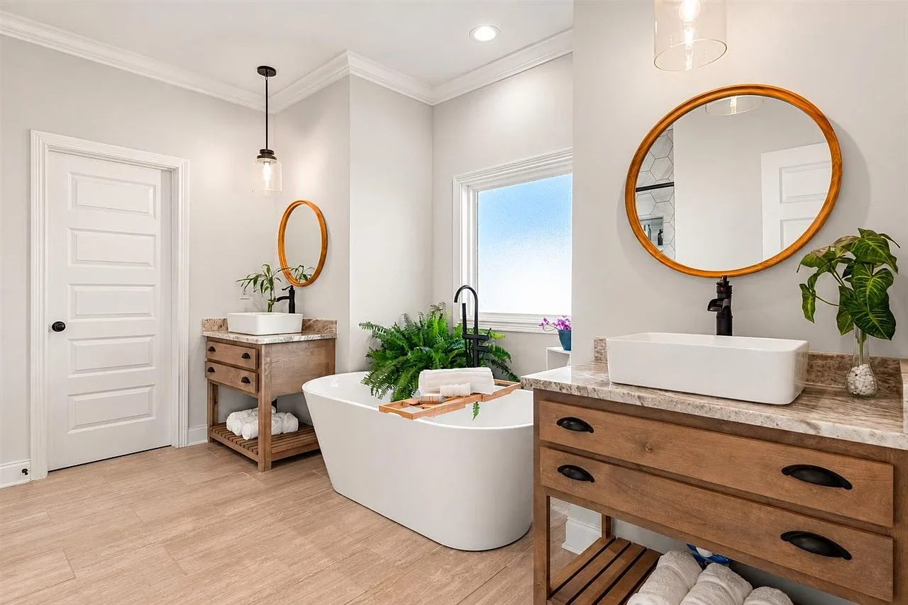 Primary bath with a freestanding soaking tub, wood vanity consoles, and matte black fixtures