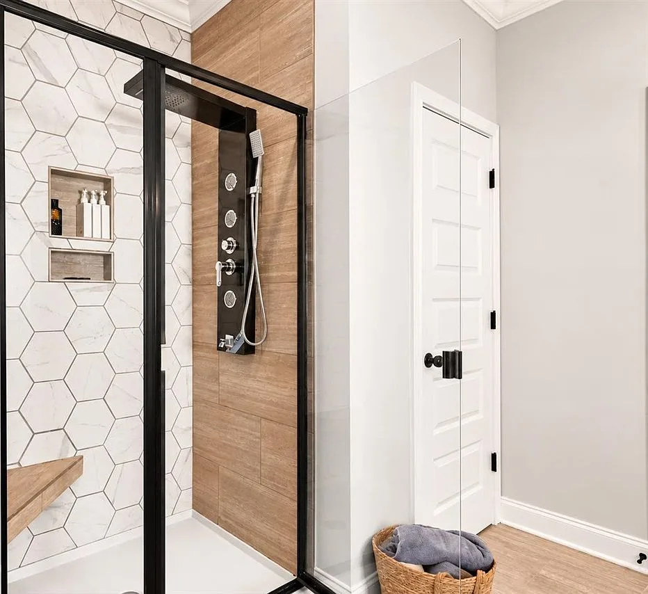 Walk-in shower with hexagonal tile, wood-look accent tile, and a black-framed glass enclosure