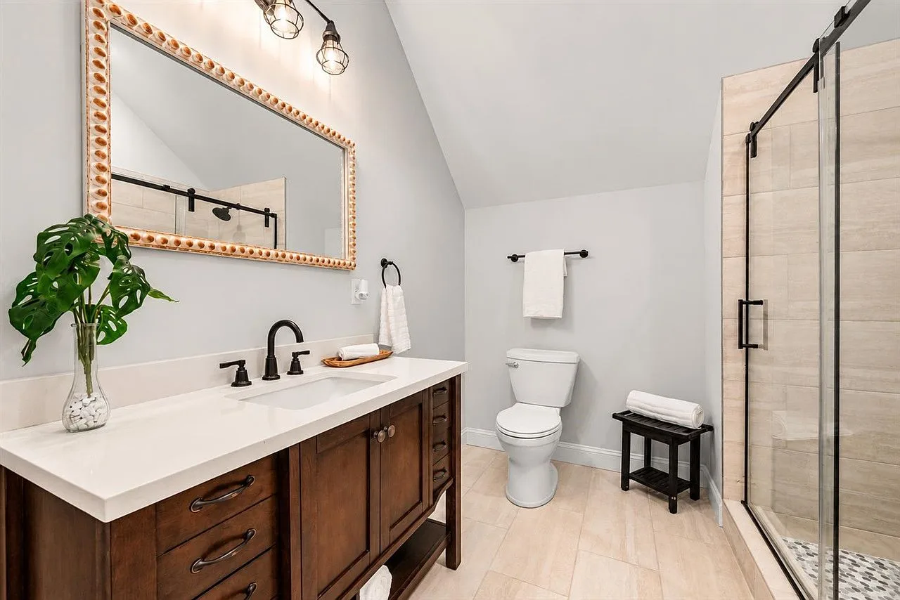 Bathroom with a dark vanity, glass shower door, and warm neutral tile