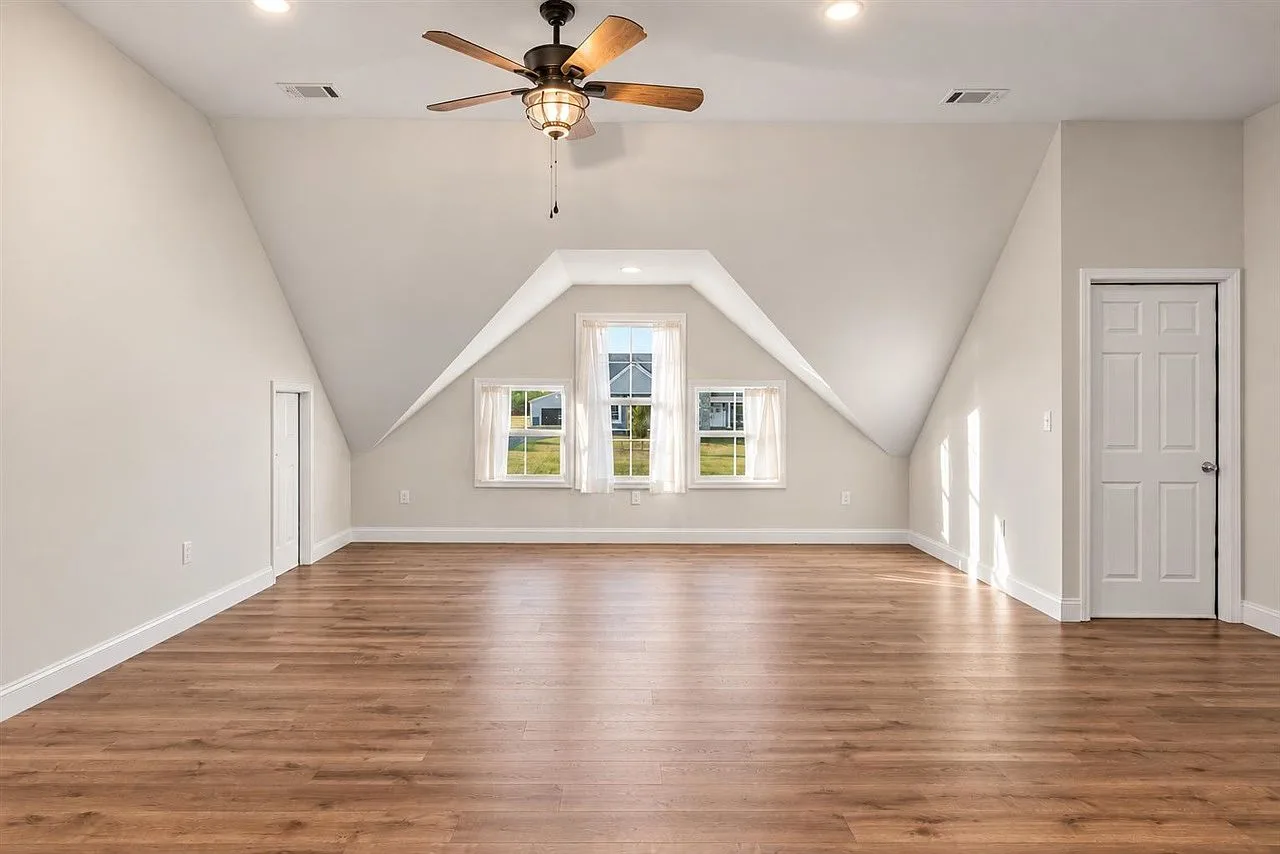 Upstairs bonus room with slanted ceilings, three windows, and soft daylight