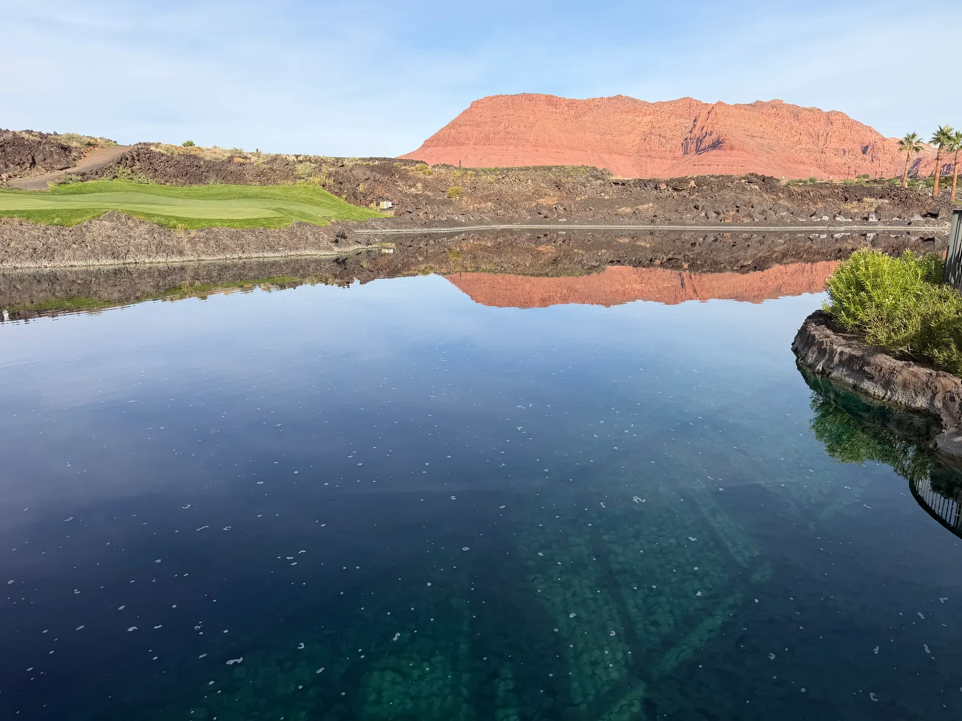 Scenic pond water feature at Black Desert framed by lava rock terrain and red rock cliffs
