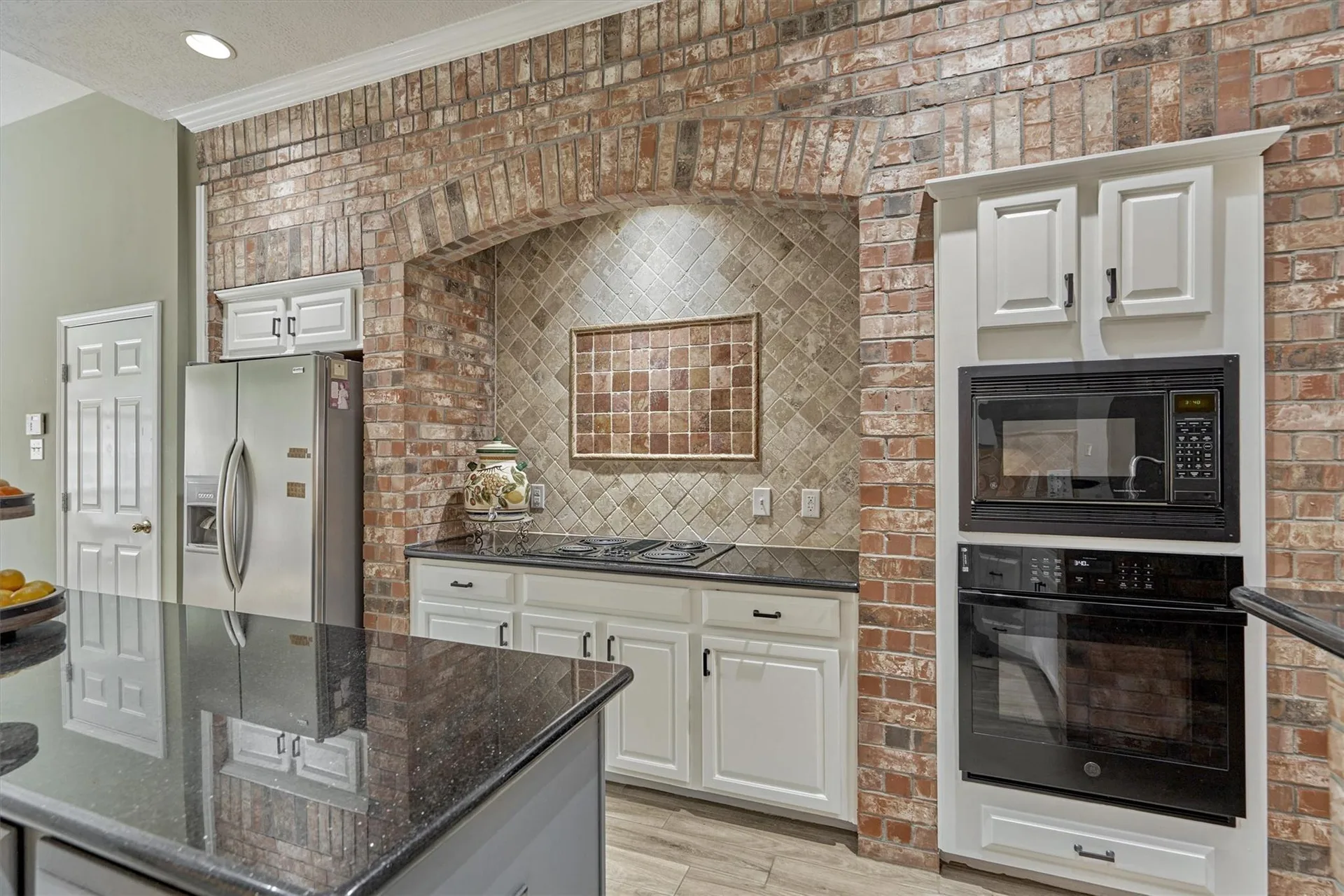 Kitchen with exposed brick arched niche, white cabinetry, granite countertops, and island