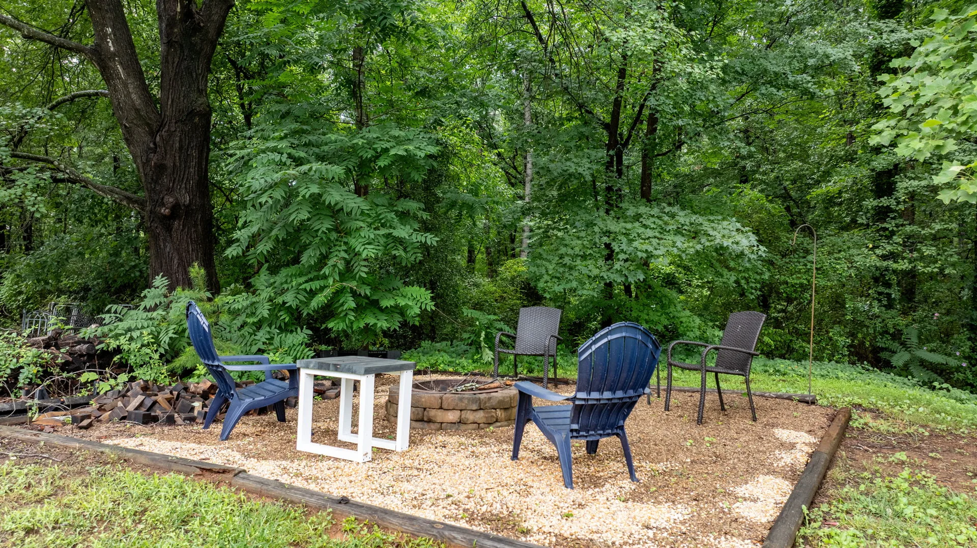 Fire pit patio bordered by landscape timbers, surrounded by mature shade trees