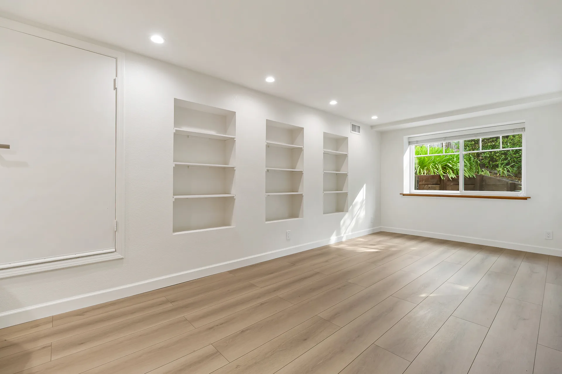 Bedroom with three built-in wall niches and a window, light hardwood floors