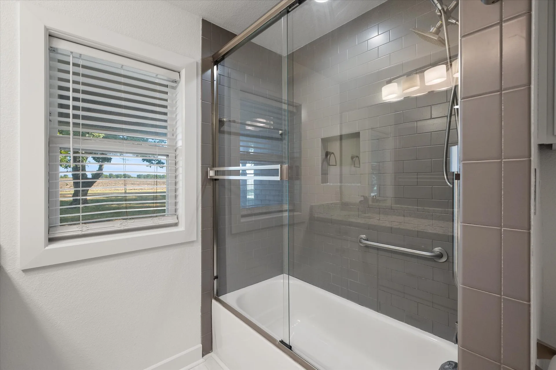 Renovated bath with gray subway tile surround and a glass sliding shower door