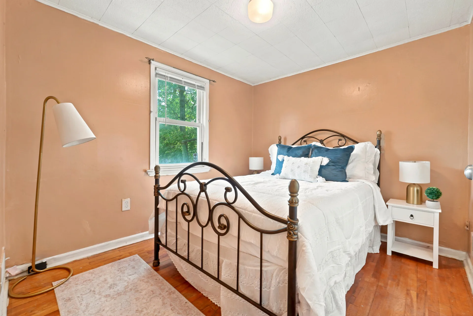First-floor bedroom with beige walls, hardwood flooring, and bright window light
