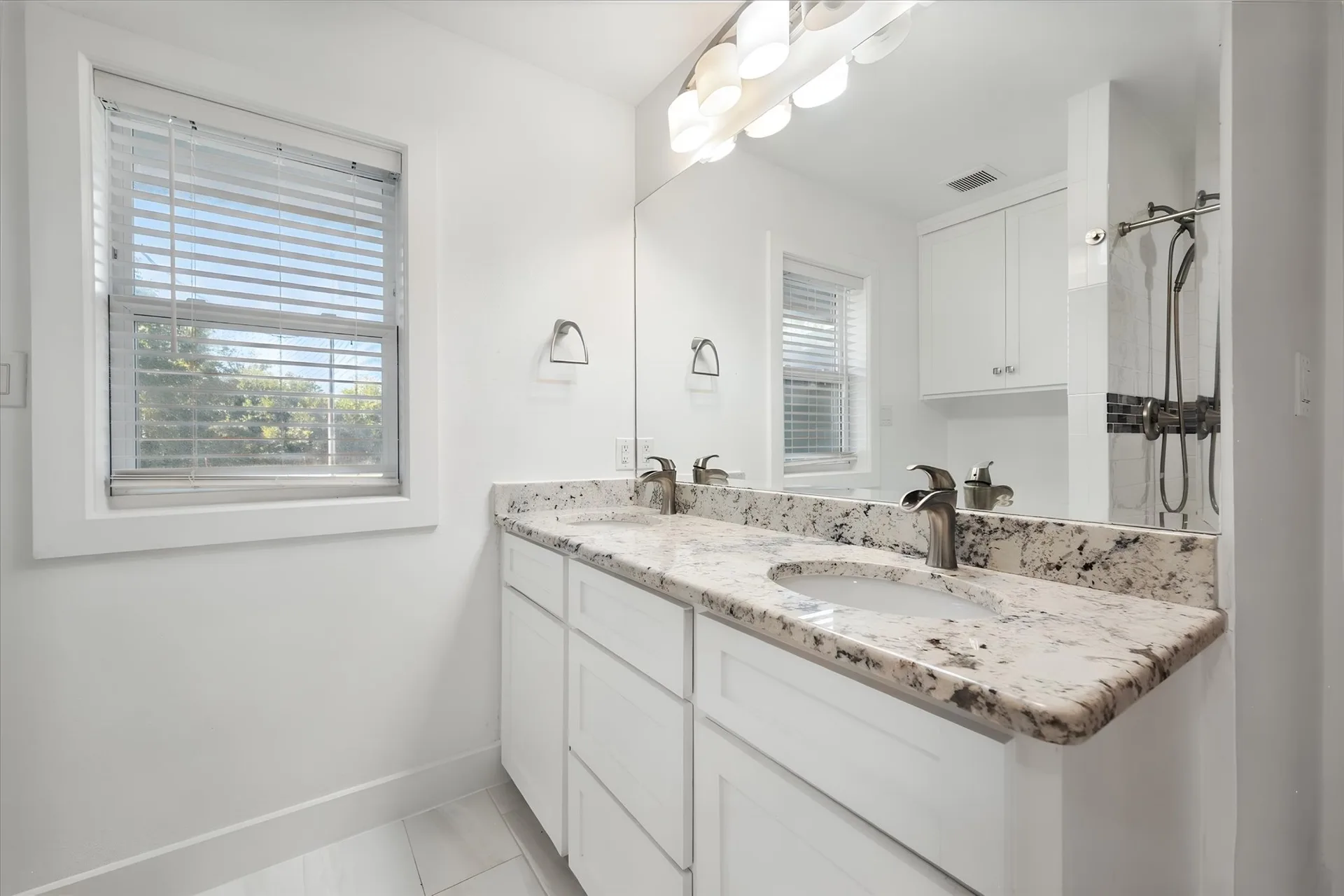Updated dual-vanity bathroom with granite counters, a large mirror and tiled floor